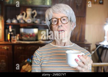 Eine mürrische ältere Frau, die eine Kaffeetasse hält Stockfoto
