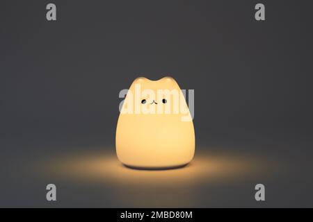 Katzenförmige Lampe auf dunklem Hintergrund. Süße katzenförmige Nachtlampe aus Silikon auf weißem Hintergrund in einem dunklen Raum. Stockfoto