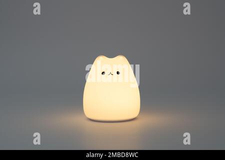 Katzenförmige Lampe auf dunklem Hintergrund. Süße katzenförmige Nachtlampe aus Silikon auf weißem Hintergrund in einem dunklen Raum. Stockfoto