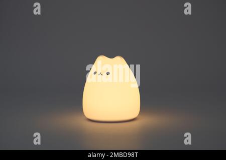 Katzenförmige Lampe auf dunklem Hintergrund. Süße katzenförmige Nachtlampe aus Silikon auf weißem Hintergrund in einem dunklen Raum. Stockfoto