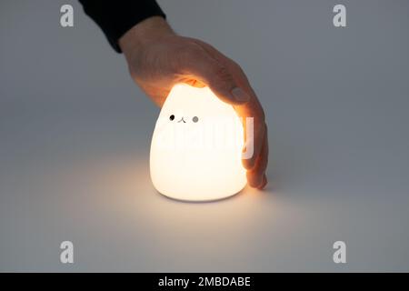 Katzenförmige Lampe auf dunklem Hintergrund. Süße katzenförmige Nachtlampe aus Silikon auf weißem Hintergrund in einem dunklen Raum. Stockfoto