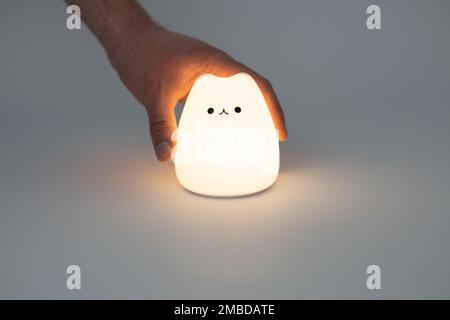 Katzenförmige Lampe auf dunklem Hintergrund. Süße katzenförmige Nachtlampe aus Silikon auf weißem Hintergrund in einem dunklen Raum. Stockfoto