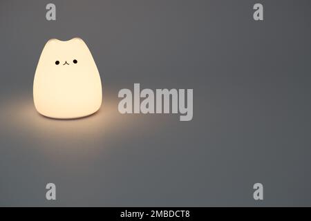 Katzenförmige Lampe auf dunklem Hintergrund. Süße katzenförmige Nachtlampe aus Silikon auf weißem Hintergrund in einem dunklen Raum. Stockfoto