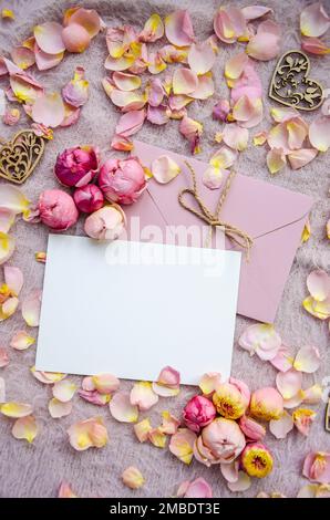 Gestalte einen rosafarbenen Umschlag mit unbeschrifteter Karte, dekorativen Holzherzen, Rosenblättern und Knospen auf pinkfarbenem Strickhintergrund. Hintergrund zum Valentinstag und Copy Spac Stockfoto