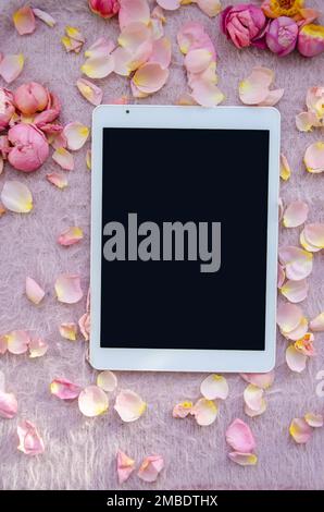 Digitales Tablet, leerer Bildschirm mit kleinen Blütenblättern auf pinkfarbenem gestricktem Hintergrund. Hintergrund zum Valentinstag und Kopierbereich für Ihren Text. Stockfoto