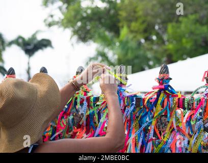 Salvador, Bahia, Brasilien - 06. Januar 2023: Eine katholische Frau legt während einer Open-Air-Messe in ein Band auf das Eisengeländer der Kirche Senhor do Bonfim Stockfoto