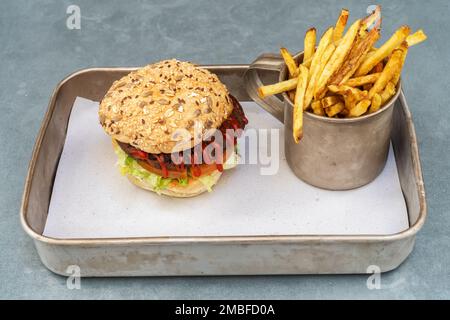 Vegetarischer Hamburger aus Bohnen, Gemüse und Ketchup-Brötchen und gebratenen Kartoffeln in einer alten Tasse auf einem Metalltablett. Stockfoto