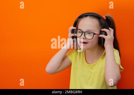 Mädchen mit Down-Syndrom hört Musik. Orangefarbener Hintergrund Stockfoto