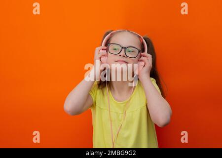 Mädchen mit Down-Syndrom hört Musik. Orangefarbener Hintergrund Stockfoto