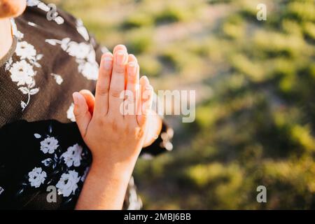 Unerkennbare Gläubige Person mit betenden Händen bei Sonnenuntergang auf dem Feld. Unterwerfung an Gott im Gebet. Stockfoto