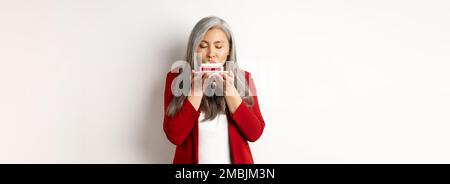 Bild von lustigen asiatischen Senior Dame schnüffeln leckeren Kuchen, Geruch Dessert mit zufriedenen Gesicht, über weißem Hintergrund stehen Stockfoto