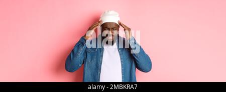 Bekümmerte schwarze Mann mit Kopfschmerzen, berühren Kopf und Grimacing mit betroffenen Gesicht, stehen über rosa Hintergrund Stockfoto
