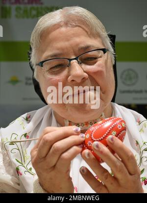 Berlin, Deutschland. 20. Januar 2023. Helene Herberg von der Vereinigung "Landurlaub in Sachsen" färbt während der Internationalen Grünen Woche (IGW) am Stand in der Ausstellungshalle Sachsen ein Ei mit einer Feder und rotem Wachs. Die weltweit größte Messe für Lebensmittel, Landwirtschaft und Gartenbau existiert seit 1926, und seit 1996 findet auch die Messe Heim-Tier & Pflanze im Rahmen der Messe statt. Die diesjährige Ausgabe endet am 29.01.2023. Kredit: Soeren Stache/dpa/Alamy Live News Stockfoto