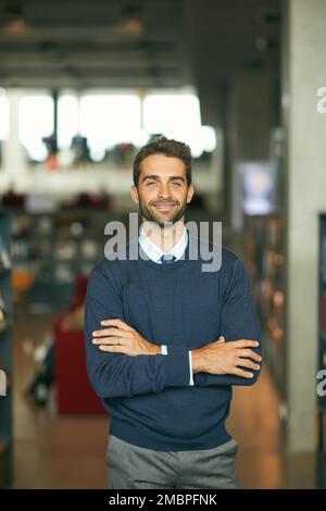 Alles, was ich wissen muss, ist in dieser Bibliothek. Verkürztes Porträt eines gutaussehenden jungen Geschäftsmanns, der mit gekreuzten Armen in einer Bibliothek steht. Stockfoto