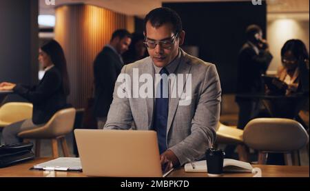 Ein Mann, der Pläne hat, wird sicher Erfolg haben. Ein junger Geschäftsmann, der nachts in einem Büro an einem Laptop arbeitet. Stockfoto