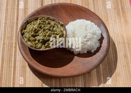 Kuherbseneintopf, eine traditionelle afrikanische Delikatesse aus Kuherbsenblättern, Kokosmilch und Erdnussmehl, serviert auf einem Bett aus flauschigem weißem Reis Stockfoto