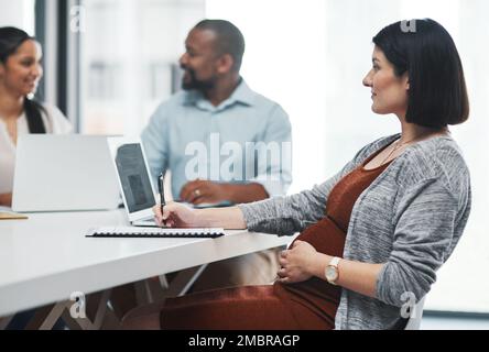 Mit einem Brötchen im Ofen jonglieren. Eine schwangere junge Geschäftsfrau, die ein Team-Meeting in einem modernen Büro abhält. Stockfoto