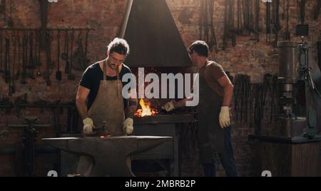 Wir arbeiten gut unter Druck. Zwei Metallarbeiter, die in einer Schweißwerkstatt arbeiten. Stockfoto