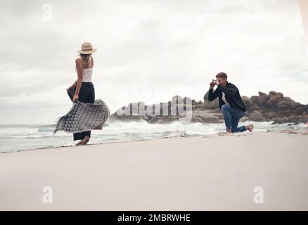 Ich liebe es, wenn sie für mich modelt. Ein Mann, der Fotos von seiner Freundin macht, während er Zeit am Strand verbringt. Stockfoto