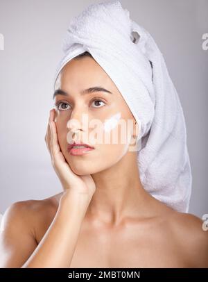 Frau, Kopftuch und Creme für Kosmetik, Make-up und Gesichtsentgiftung auf grauem Studiohintergrund. Junge Frau, Frau und organische Gesichtspflege zur Behandlung, klar Stockfoto