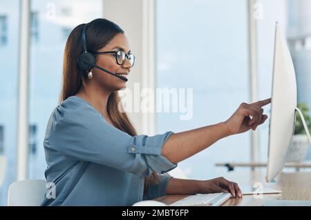 Die Art ihrer Arbeit erfordert gute Kommunikationsfähigkeiten. Eine junge Geschäftsfrau, die ein Headset trägt, während sie an einem Computer im Büro arbeitet. Stockfoto