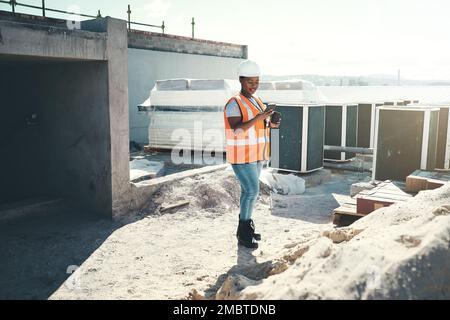 Die Produktivität nimmt eine Pause ein. Eine junge Frau, die während einer Kaffeepause auf einer Baustelle ein Smartphone benutzt. Stockfoto