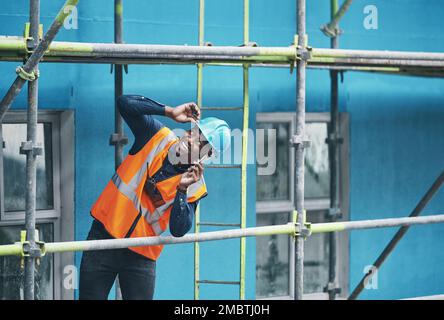 Ich sehe dich da oben. Ein junger Mann, der auf einer Baustelle telefoniert. Stockfoto