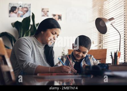 Hausaufgaben als Team angehen. Ein süßer kleiner Junge, der eine Schulaufgabe mit seiner Mutter zu Hause erledigt. Stockfoto