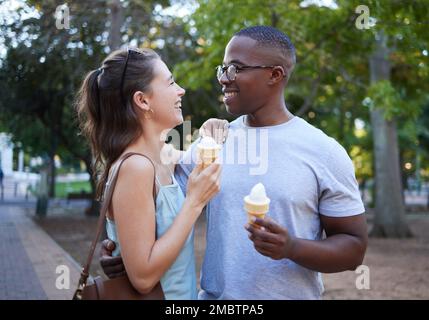 Liebe, Eis oder ein paar Freunde umarmen sich in einem Park bei einem romantischen Date in der Natur in einer zwischenrassischen Beziehung. Verbindender, entspannter Schwarzer und glücklich Stockfoto