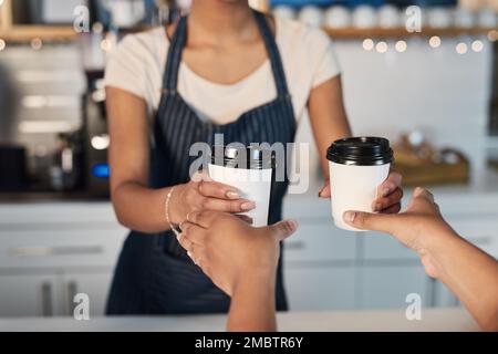 Ein weiterer geschäftiger Tag in ihrem Kaffeehaus. Nahaufnahme eines Baristas, der einem Gast in einem Café Kaffee serviert. Stockfoto