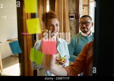 Eine Gruppe junger Geschäftsleute, die Ideen auf einer Glasplatte im Gemeinschaftsarbeitsbereich planen Stockfoto