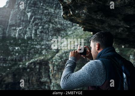 Die unvergessliche Ansicht einfangen. Ein junger Mann, der während einer Wanderung Fotos macht. Stockfoto