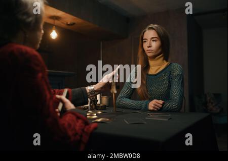 Junge Frau, die beim reifen alten Zigeuner-Taro-Leser um Rat bittet Stockfoto