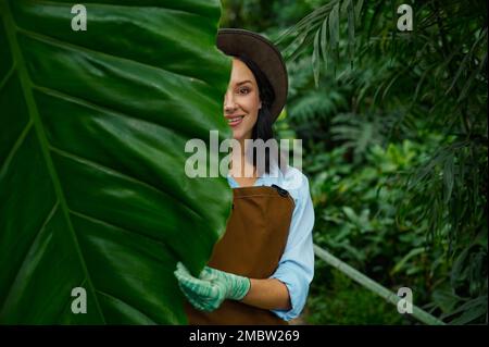 Porträt einer wunderschönen Gärtnerin, die durch üppiges Laub in die Kamera schaut Stockfoto
