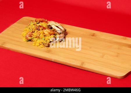 Gericht aus Valencia Spanien Arroz a la Paella auf einem Holzbrett mit rotem Hintergrund, zubereitet mit Safran, Meeresfrüchten, Garnelen und Gemüse Stockfoto