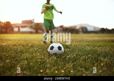 Schieß für deine Ziele. Nahaufnahme eines kleinen Jungen, der Fußball auf einem Sportplatz spielt. Stockfoto