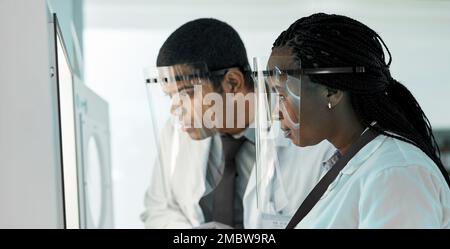 Ich gehe zur Laborarbeit. Zwei Wissenschaftler tragen Gesichtsschutz, während sie in einem Labor zusammenarbeiten. Stockfoto