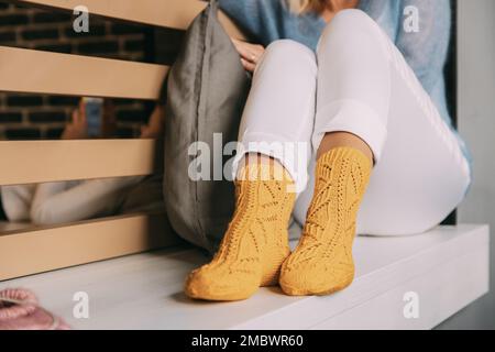 Tröstende, gemütliche Frau in gestrickten wintergelben Socken Stockfoto