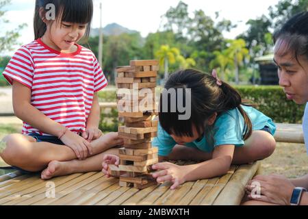 Aufgeregte Kinder und mom spielen gemeinsam im Park ein Holzblockspiel im Jenga Tower. Glückliche Familie mit Kindern, die gemeinsam Wochenendaktivitäten genießen. Stockfoto