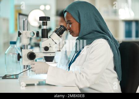 Jede Idee durchläuft gründliche Experimente. Ein junger Wissenschaftler, der ein Mikroskop in einem Labor benutzt. Stockfoto