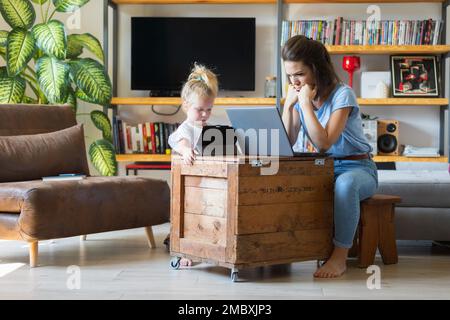 Junge Frau und kleines Mädchen starren auf ihre sehr konzentrierten Bildschirme im Wohnzimmer. Lernen, arbeiten oder spielen sie Schach? Stockfoto