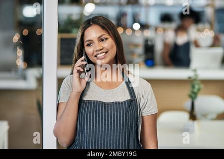 Ein weiterer erfolgreicher Tag. Eine junge Frau, die telefoniert, während sie in einem Café arbeitet. Stockfoto