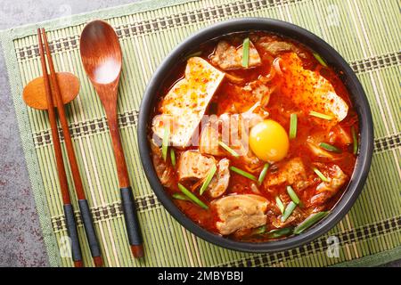 Scharfer, weicher Tofu-Eintopf mit Kimchi und Schweinebauch auf der Schüssel auf dem Tisch. Horizontale Draufsicht von oben Stockfoto
