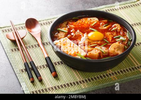 Scharfer, weicher Tofu-Eintopf mit Kimchi und Schweinebauch auf der Schüssel auf dem Tisch. Horizontal Stockfoto