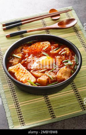 Sundubu Jjigae ist ein koreanischer Eintopf, der aus weichem Tofu, Kimchi, Schweinebauch, Zwiebeln und Gewürzen auf der Schüssel auf dem Tisch zubereitet wird. Vertikal Stockfoto