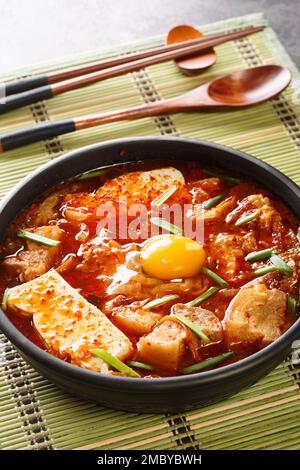 Sundubu Jjigae scharfe Kimchi Soft Tofu Eintopf-Nahaufnahme auf der Schüssel auf dem Tisch. Vertikal Stockfoto