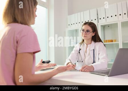 Arzt kommuniziert mit der Patientin in der Klinik und hört sich ihre Beschwerden an Stockfoto