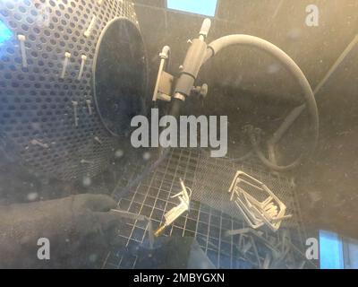 Schusssprengen. Sprengung des Modells auf 3D-Drucker aus Polyamidpulver. Ein Arbeiter in versiegelten Gummihandschuhen reinigt den Gegenstand durch Schusssprengen in einer Schusssprengring-Kammer. Industriemaschinen Stockfoto