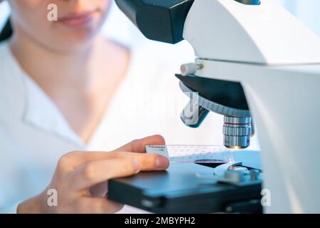 Junge Frau im medizinischen Labor, die Biopsieproben unter dem Mikroskop untersucht Stockfoto