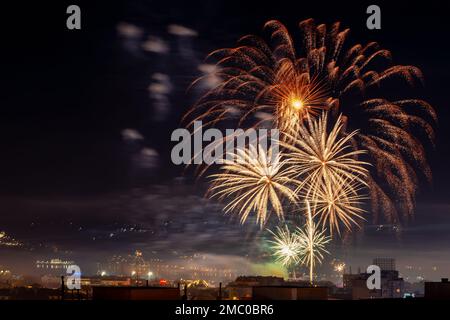Festliches Feuerwerk am Nachthimmel. Gelbes orangefarbenes Feuerwerk, Explosionen über der Stadt, um Feiertage zu feiern. Pyrotechnik für das Fest-Konzept. Stockfoto